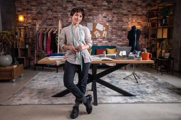 Fashion and clothing designer beautiful woman at her clothing atelier and tailoring posing in front of the camera she holding her tailoring scissors and looking straight to the camera. Portrait