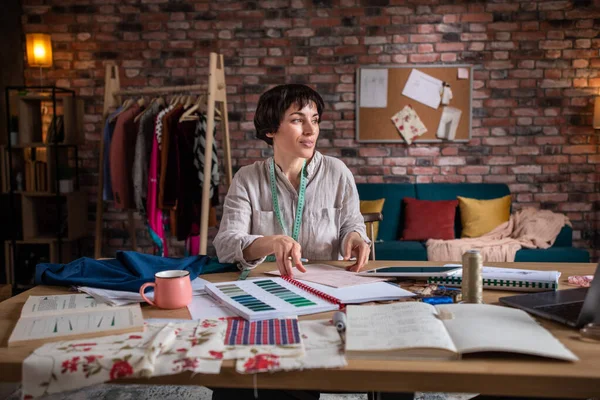 Concept of small business tailoring fashion people talented dressmaker woman with a pretty smile take her sketches from the work table came to the sew mach.ine and start to sewing some fabrics.