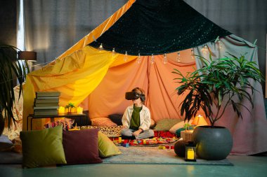 The boy chilling together inside a blanket fort while playing with a virtual reality headset and laughing.