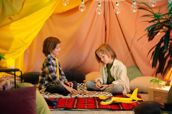 Two young boys with long hair are high fiving each other and seem really happy to be in an indoor tent.