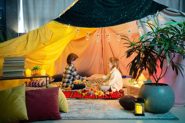 Two really young cute and charming boys are having fun and high fiving eachother in a big comfy indoor tent.