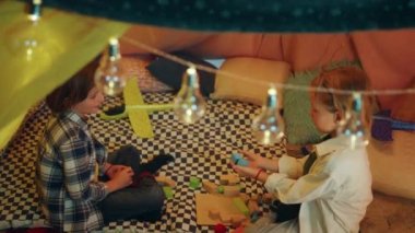 Two boy buddies are playing with building blocks together inside an enormous and lively blanket tent.