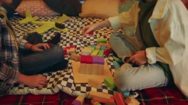 A shot of two boys sitting down comfortably inside a gleeful looking tent with indoor plants and books on the outside of it, they re having fun together. 4k