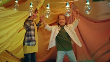 In an electric atmosphere two young boys are smiling and dancing with each other inside a glorious blanket fort.