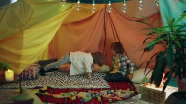 Two little boys are hanging out inside a comfortable blanket tent and one of the boys is doing push-ups while the other watches in encouragement. 4k
