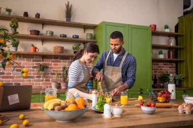 Handsome guy and Caucasian lady together in the morning take the breakfast together at the kitchen island at home they drink some fresh orange juice.