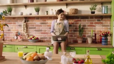 Large modern kitchen happy woman using laptop to work while her husband brings a good hot tea and they take the break together and drink some tasty tea. 4k