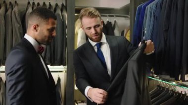 In the luxury suit shop man groom try to choose the best suit for the wedding the consultant guy try to show more suits form the new collection. 4k