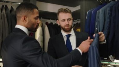 In the modern suit shop businessman try to choose a good and couture suit from the new collection he discussing with the design man. 4k