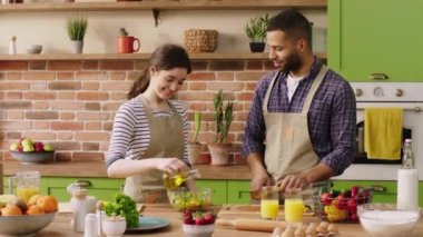 Multiethnic couple very good looking at the large spacious kitchen preparing the breakfast together they mix the fresh salad smile very lovely and looking at each other. 4k