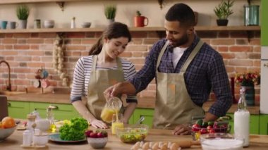 Good looking guy and pretty female very charismatic couple multiracial together at the kitchen island enjoy the breakfast time they drink some fresh orange juice and smiling large. 4k