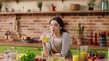 Very beautiful lady drink some fresh juice in front of the camera at the kitchen island at home then looking to the camera and smiling large. 4k