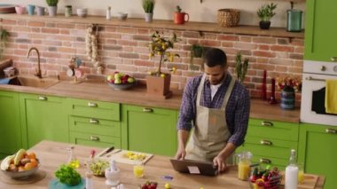 Happy and attractive guy while preparing some food make a video call from the laptop and start a conversation with someone online. 4k