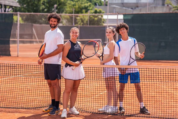 Group of friends having fun standing together with rackets on the tennis court.