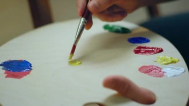 Painter man is mixing two colours of yellow and pink on a colour palette to form a new colour.