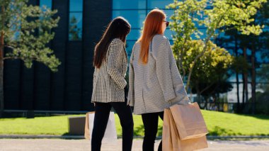 Modern kasabanın ortasında, iki karizmatik ve çekici kadın ve birkaç çevre çantasıyla birlikte yürüyorlar ve tartışıyorlar..