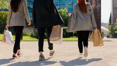 Good looking multiracial group of colleagues from work have a good shopping they walking down on the street holding some eco shopping bags taking video from the back. Portrait