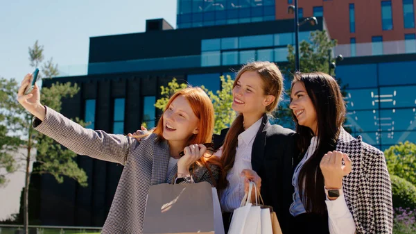 In front of the camera group of young women after their work day taking some selfies with smartphone beside of amazing modern business building.