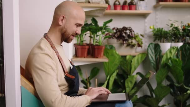 自分の花屋で起業家の男は 彼が階段に座って大きな笑みを浮かべて何かを入力ノートパソコンに取り組んでいます Arriアレクサミニで撮影 — ストック動画