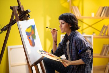 A beautiful woman artists with short hair is using her amazing art skills to paint something beautiful on the canvas in an art studio.