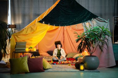 The boy are hanging out in a children s blanket tent indoors while playing with a vr headset and enjoying their time laughing together.