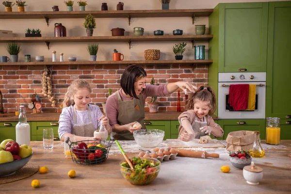 At home in a large kitchen island happy mother and her two kids daughters mixing and preparing a delicious dessert together they smiling large and enjoy the time together. Portrait