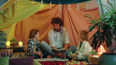 Yakışıklı bir baba ve iki genç oğlu çok modern ve rahat battaniyeleriyle hikaye kitabı okuyorlar çünkü atmosfer çok rahatlatıcı ve sevimli. 4k