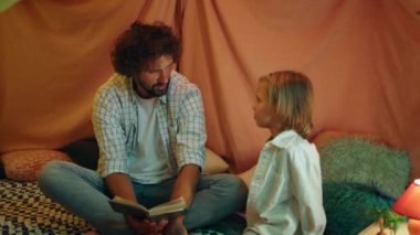 Sarışın küçük bir çocuk ve kahverengi saçlı yakışıklı bir baba birbirleriyle konuşuyor ve muhteşem battaniye kalelerinin içinde bir kitabı tartışıyorlar. 4k