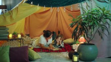 Oğluyla bağ kuran bir annenin, ona kitap okurken ve battaniye kalesinin içinde rahat kıyafetler giyip eğlenirken çekilmiş bir fotoğrafı. 4k