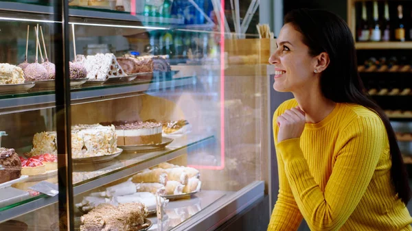 Beautiful woman customer in the bakery cafe choose a desert from the showcase fridge she is very excited.