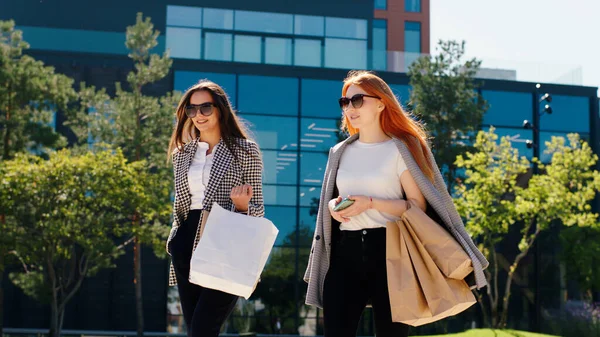 Good looking two ladies walking home from shopping holding some eco shopping bags they walking through the modern town wearing sunglasses.