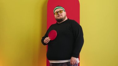 Kameranın önünde karizmatik poz veren yakışıklı şişman adam raketi elinde tutuyor ve masa tenisi oynamaya hazırlanıyor. ARRI Alexa Mini 'de çekilen