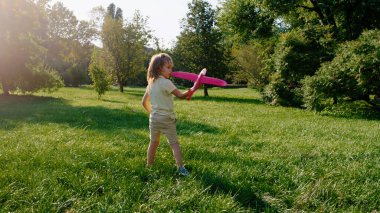 Küçük tatlı çocuk parkın ortasında uçakla sert oynuyor çimlerin arasında koşuyor..