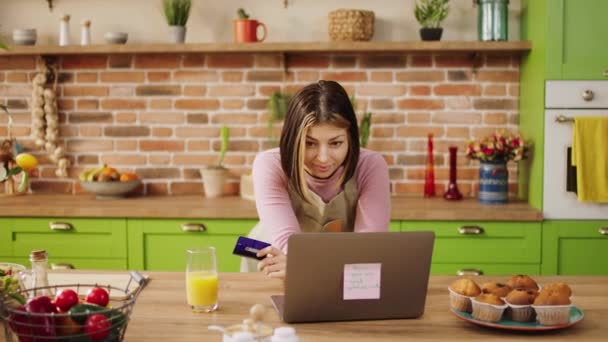 現代のキッチン幸せな家の女性は 彼女がラップトップで何かを見て 大きな笑みを浮かべてオンラインショッピングを作るためにラップトップを使用しています — ストック動画