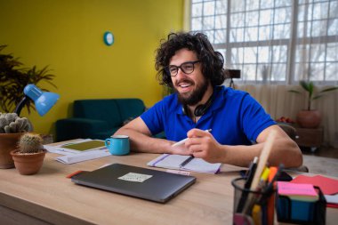 Sınıf ödevini evde yapan yakışıklı bir öğrenci. Düşünen bir yüzü var ve not defterine bazı notlar yazmak için kalemi kullanıyor..