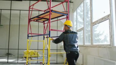 İnşaat işçisi inşaat alanında alüminyum merdiveni yuvarlıyor koruyucu başlık ve üniforma giyiyor..