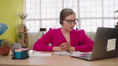 Bilgisayardan müşterisiyle çevrimiçi çalışan inanılmaz güzel bir bayan yardım asistanı. Kulaklık takıyor ve ofis merkezinde bazı şeyleri anlatıyor..