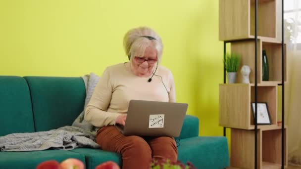 거실에 소파에 할머니는 온라인 강의를 랩탑을 사용하며 소파에 노트북을 헤드셋을 — 비디오