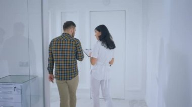 Büyük, beyaz, modern bir klinikte hasta adam hemşireyle tartışırken hemşire dinlediği bir şeyi anlatıyor..