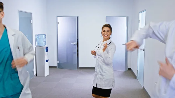 In a modern hospital corridor group of doctors and nurses dancing excited in front of the camera and smiling cute.