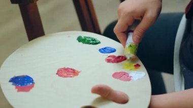 Paletine parlak sarı boya sürmek için ellerini kullanan bir adamın yakın çekimi..