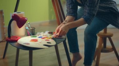 Bir ressam, tuvalini boyamaya devam edebilmek için elleriyle çok büyük bir palet tutuyor ve üzerine boya sıkıyor.