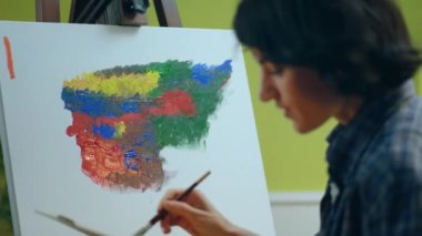 Modern ve parlak sanat atölyesindeki beyaz tuvaline modern ve görkemli bir şey çizen güzel ve cezbedici kadının yakın çekimi. ARRI Alexa Mini 'de çekilen