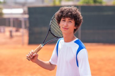 Profesyonel sporcu karizmatik yakışıklı tenisçi kavramı kameranın önünde poz veriyor gülümsüyor, raketi elinde tutuyor ve üniformasını giyiyor. Portre