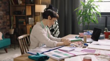 Projesinde çalışan güzel moda tasarımcısı kadın güzel modern terzi atölyesinde birkaç yeni kıyafet koleksiyonu yapıyor. 4k