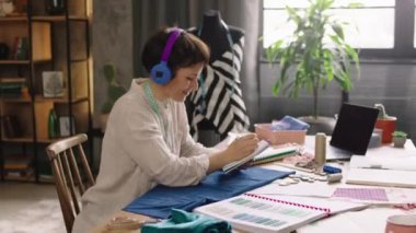 Moda atölyesi kadın moda tasarımcısının yeni koleksiyonunda çalışırken kulaklıklardan müzik dinleyip yavaş hareket ettiği güzel bir iş yeri. 4k