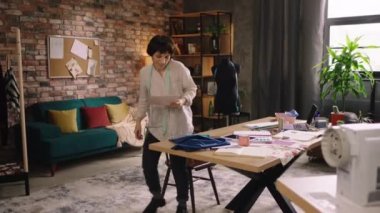 Moda ofisi çok yaratıcı güzel kadın giyim tasarımcısı yeni elbise koleksiyonunun taslaklarını alıp dikiş makinesine geldi ve kumaş dikmeye başladı. 4k