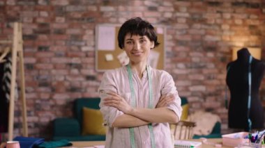 Modern terzi atölyesinde el ele tutuşurken kameranın önünde poz veren terzi kadın portresi. ARRI Alexa Mini 'de çekilen