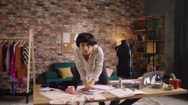 Terzi atölyesindeki güzel kadın terzi masanın üzerinden atlayıp doğrudan kameraya bakarak dans ediyor ve büyük bir gülümseme sergiliyor. 4k