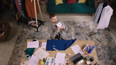 Üst Manzara. Bir adam tavana kağıt bir uçak fırlatıyor ve kumaşı ölçerken kafasını müziğe doğru sallayarak işine geri dönüyor.